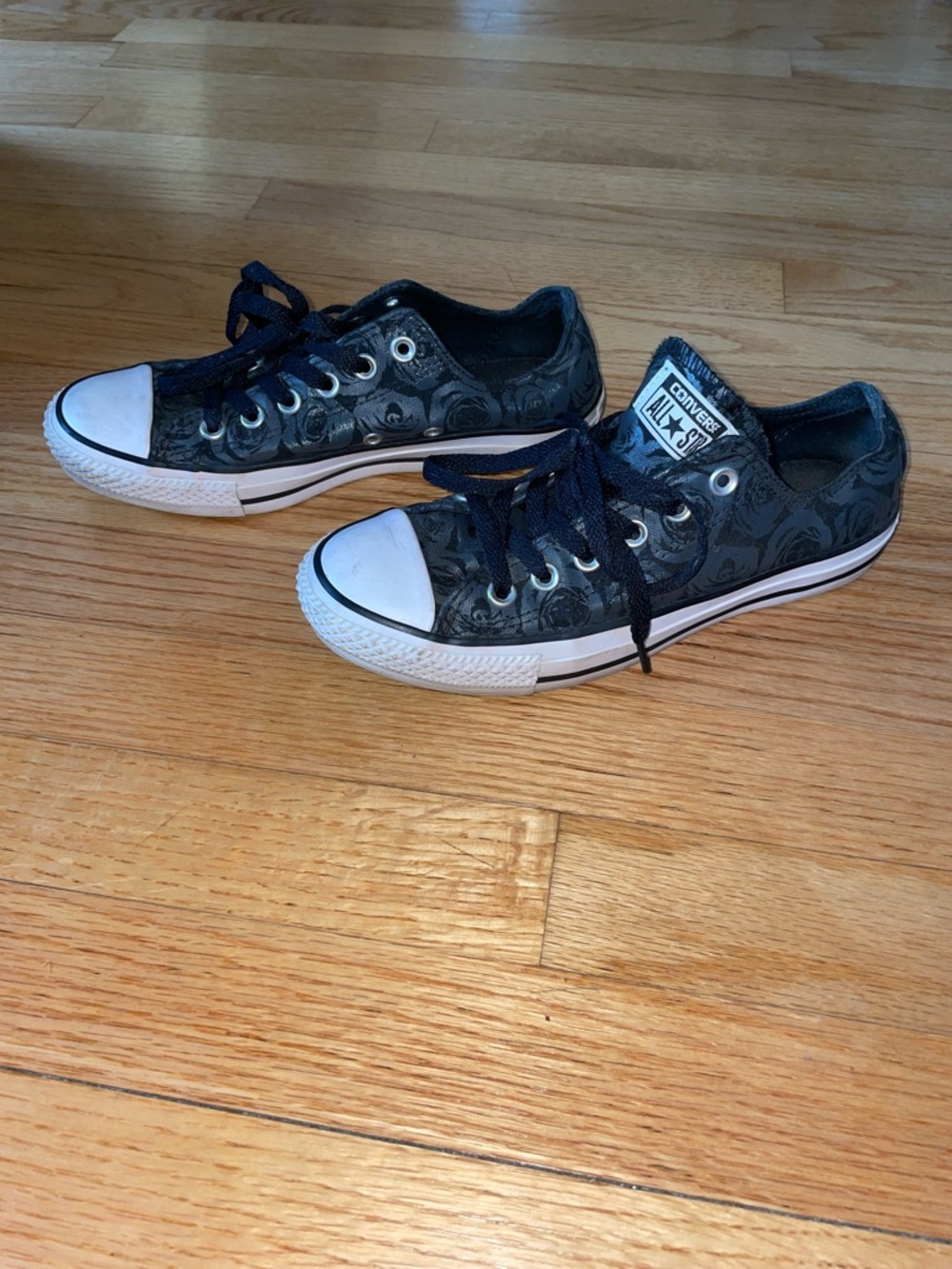 Black, low-top Converse sneakers with floral pattern.